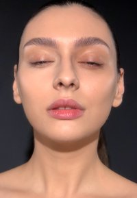 Nahaufnahme eines Gesichts mit glatter, heller Haut; gepflegte Augenbrauen; gedämpfter rosa Lippenstift; neutraler Hintergrund; keine sichtbaren Accessoires.