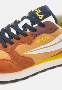 Orange and brown sneaker with navy laces, white logo, and yellow accents. Features a mix of suede and synthetic materials with textured details.