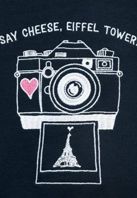 Design brodat care prezintă o cameră cu o inimă și o fotografie a Turnului Eiffel, subtitlul spune "Spune brânză, Turnul Eiffel."