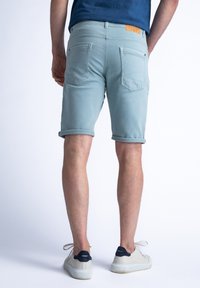 Pantalones cortos de mezclilla azul claro con los bajos doblados, que cuentan con dos bolsillos traseros, detalles cosidos y una etiqueta de cuero marrón en la cintura.