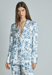 Set di giacca e pantaloni con stampa floreale, caratterizzato da una base bianca con fiori blu, rever a punta e due tasche frontali. Tessuto liscio e vestibilità su misura.