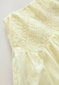 Robe en coton jaune à manches courtes, ornée de panneaux en dentelle texturée, de détail en pinces verticales et d'une jupe froncée avec un drapé doux.