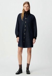 Robe en denim foncé avec un devant boutonné, des manches longues bouffantes et une coupe décontractée, ornée de boutons dorés et d'un col simple.