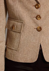 Bruine gestructureerde blazer met een getailleerd ontwerp, voorzien van vier grote bruine knopen en een zijzak met knoopsluiting.