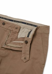 Chino in cotone marrone chiaro con zip, chiusura con bottone, due tasche frontali e un'etichetta decorativa in vita con scritte dorate.