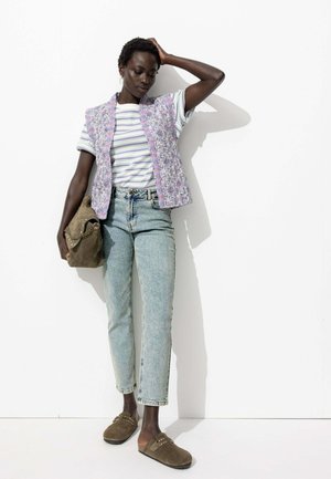 Gilet sans manches à motif floral lavande sur un t-shirt rayé. Jean taille haute bleu clair et sabots marron avec des clous. Sac olive.
