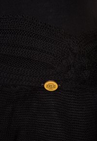Schwarzer Strickstoff mit einer strukturierten Musterung. Enthält ein kleines rundes goldenes Abzeichen mit dem Schriftzug "KHUJO", das die Markenidentität hervorhebt.