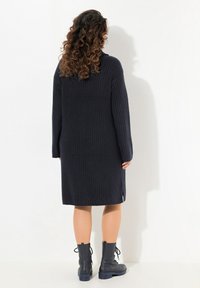 Robe en tricot bleu marine foncé, avec une texture côtelée, des manches longues et des fentes latérales, associée à des bottines noires avec des détails en dentelle.