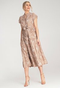 Hellbraunes Midi-Kleid mit weißen Blumenmustern, kurzen Ärmeln und einem taillierten Saum. Es hat einen lockeren Schnitt und einen gestuften Rock.