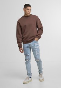 Pruun kapuutsiga särk ümmarguse kaelusega, pika varrukaga, koos helesiniste kulunud teksadega, millel on valge tikand. Rõivastuse lõpetab mugav jalats.