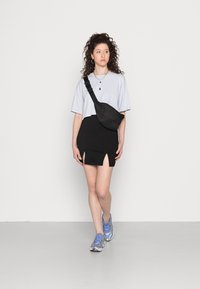 T-shirt cropped azul claro, saia mini preta com fendas laterais, bolsa slinger preta, joias prateadas e sapatilhas cinzas com detalhes azuis.