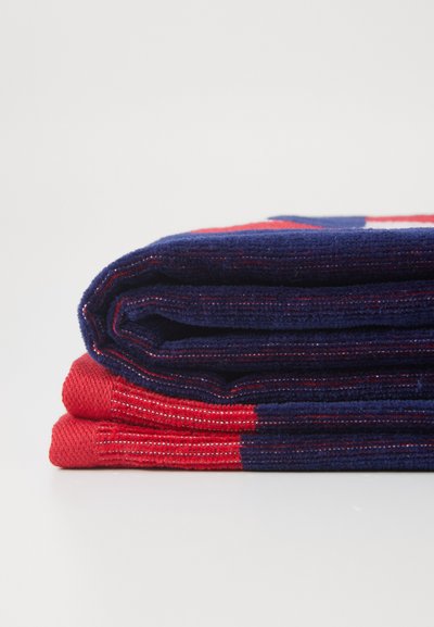 Deux serviettes pliées présentent un schéma de couleurs bleu marine et rouge avec une texture striée. Les bords affichent des motifs contrastés et une finition nette.