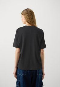 Black cotton t-shirt with a relaxed fit, short sleeves, and a crew neckline, paired with blue baggy denim pants.