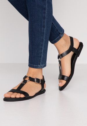 Sandales en cuir noir avec des sangles réglables et une semelle plate. Présentent des éléments en métal et un design ouvert au niveau des orteils. Assorties avec un denim foncé.