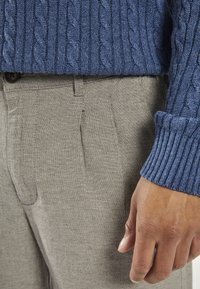 Blue cable-knit sweater with ribbed cuffs paired with light gray textured trousers, featuring two front pleats and a button closure.