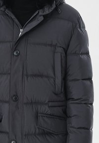 Padded czarna kurtka z zamkiem z przodu, dwoma kieszeniami zapinanymi na guziki i kapturem. Oferuje poziome przeszycia oraz gładką, trwałą fakturę materiału.