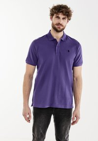 Polo violet en coton. Présente un col classique, des manches courtes et un petit logo noir sur la poitrine gauche. Coupe décontractée.