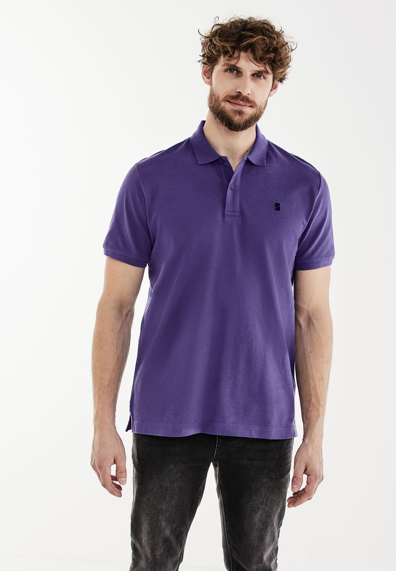 Polo violet en coton. Présente un col classique, des manches courtes et un petit logo noir sur la poitrine gauche. Coupe décontractée.