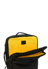 Mochila negra con asa superior y bolsillo frontal abierto que muestra un interior amarillo brillante y compartimentos organizadores.
