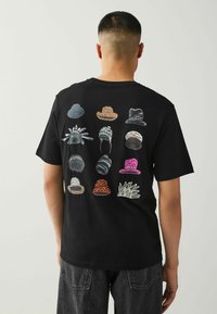 T-shirt nera con una grafica di vari cappelli in diverse forme, colori e texture stampata sul retro.