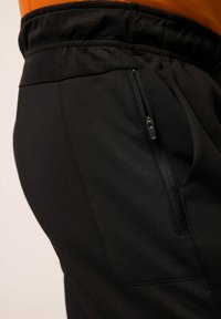 Pantalones deportivos negros con una textura suave, que presentan una cinturilla elástica y un bolsillo lateral con cremallera. El diseño es elegante y ajustado al cuerpo.