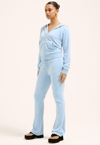 Ljusblå velour träningsdräkt med en tajt zip-up huvtröja och matchande joggers. Har framfickor och gyllene dragkedjeaccenter. Svarta plattformssandaler.