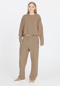 Korte bruine sweatshirt met lange mouwen, gecombineerd met bijpassende bruine joggingbroek. Beide zijn gemaakt van zachte, gladde stof met een elastische tailleband.