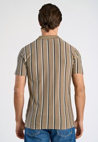 Kortärmad pikétröja i beige med vertikala svart- och vittstrimmor. Har en ribbad krage och mjukt, texturerat tyg.