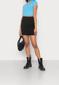 Sininen lyhyt t-paita, musta ribattu minihame, mustat nauhakiinnityssaappaat ja tikattu musta käsilaukku. Yksinkertainen ja moderni muotoilu.