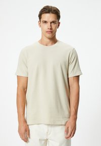 Beige bomulds t-shirt med rund halsudskæring, korte ærmer og tekstureret overflade. Kombineret med lyse bukser i et minimalistisk design.