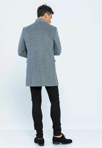 Grau-wollmischmantel mit taillierter Passform, Rückenschlitz und seitlichen Taschen, kombiniert mit schwarzen Slim-Fit-Jeans und schwarzen Schuhen.
