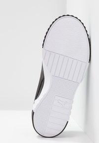 Black and white sneaker showing a textured rubber sole with a grip pattern, smooth upper material with a sleek design, and branding detail.