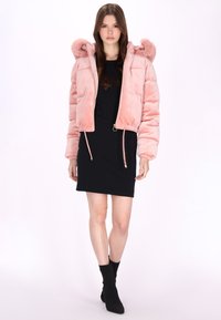 Różowa pikowana kurtka bombka z futrzanym kapturem, z elastycznym dołem i ściągaczami przy rękawach, noszona na czarnej sukience i za kostką butach.