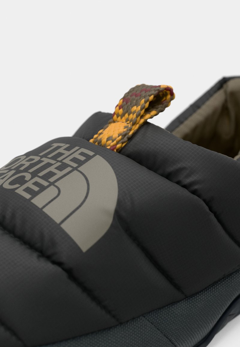 Sort polstret sko med The North Face-logo. Har en tekstureret overflade, en grå vævet trækstrop og et letvægtsdesign.