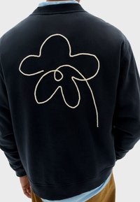 Felpa navy con un grande design floreale ricamato in beige sulla schiena; realizzata in un tessuto morbido con una vestibilità rilassata e colletto a costine.