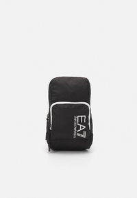 Zaino nero con dettagli bianchi, tasca frontale con zip e logo stampato. Realizzato in tessuto resistente, presenta una forma rettangolare compatta.