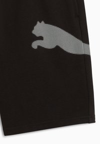 Tissu noir avec une silhouette blanche en pointillés d'un puma sautant vers la droite près d'une couture latérale.