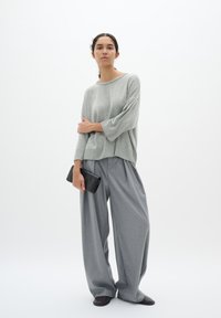 Light gray oversized sweater with three-quarter sleeves, paired with loose gray trousers and a black clutch. Smooth fabric with minimal texture.