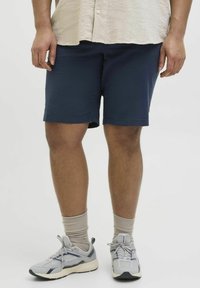 Blaue Shorts aus weichem Material, mit einem schlichten Design, geradem Schnitt und Seitentaschen. Kombiniert mit grauen Sneakern und Knöchelsocken.