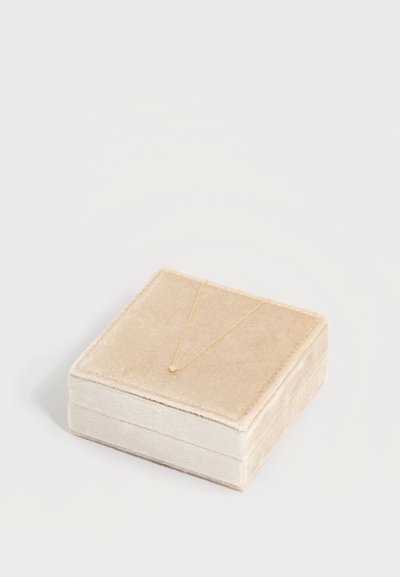 Μπεζ βελούδινο κουτί κοσμημάτων με μια λεπτή χρυσή αλυσίδα και ένα μικρό κρεμαστό κόσμημα πάνω του.