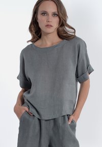 Grijze linnen top met opgerolde korte mouwen, een losvallende pasvorm en een ronde halslijn. Gladde textuur, minimale details, gecombineerd met bijpassende shorts.