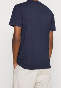 Granatowa bawełniana koszulka z krótkim rękawem i okrągłym dekoltem, z kontrastowymi szwami na mankietach i dolnym brzegu. Luźny krój.