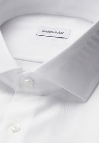 Camicia bianca con motivo a spina di pesce, materiale in cotone, colletto a doppio bottone e una leggera lucentezza. Etichetta con la scritta "seidensticker."
