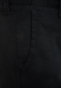 Zwarte denim broek met een rechte snit, subtiele textuur en een zijzak met tonale stiksels. Geen zichtbare branding aanwezig.