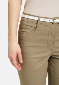 Khaki broek van gestructureerde stof, met een zijzak, gecombineerd met een witte riem met een gouden gesp.