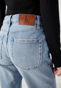 Blå denimjeans med høy midje, klassisk fem-lomme-design og et brunt lær Calvin Klein-merke på bakre livlinje.