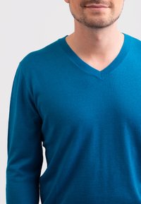 Svetr s dlouhým rukávem a výstřihem do V v jasně tyrkysové barvě, vyrobený z měkkého, hladkého materiálu s mírným leskem, s přiléhavým střihem.