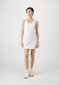 Λευκό αμάνικο φόρεμα με απλό σχέδιο, κατασκευασμένο από ομαλό ύφασμα. Έχει στρογγυλή λαιμόκοψη και πέφτει λίγο πάνω από το γόνατο.