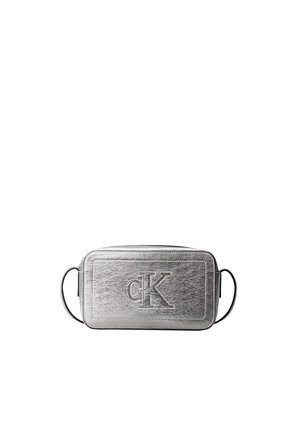 Sac bandoulière rectangulaire argenté avec logo cK embossé et fine sangle noire sur fond blanc.