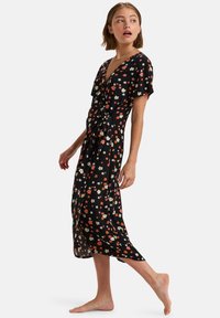 Robe noire à fleurs avec des manches courtes, ornée de fleurs colorées en rouge, blanc et jaune. Design enveloppant et ourlet à mi-genou, en tissu léger.
